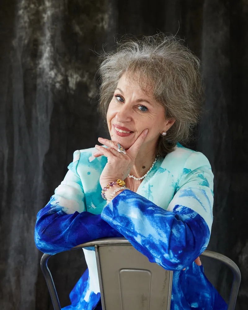 Luciana Stan smiling warmly, resting her chin on her hand, in a blue and white jacket